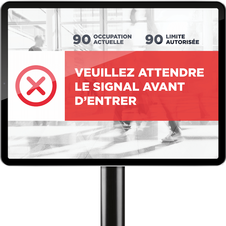 On voit une tablette sur un poteau court. Le graphique sur la tablette indique : "Veuillez attendre le signal avant d'entrer" ainsi que l'occupation actuelle et l'occupation maximale.